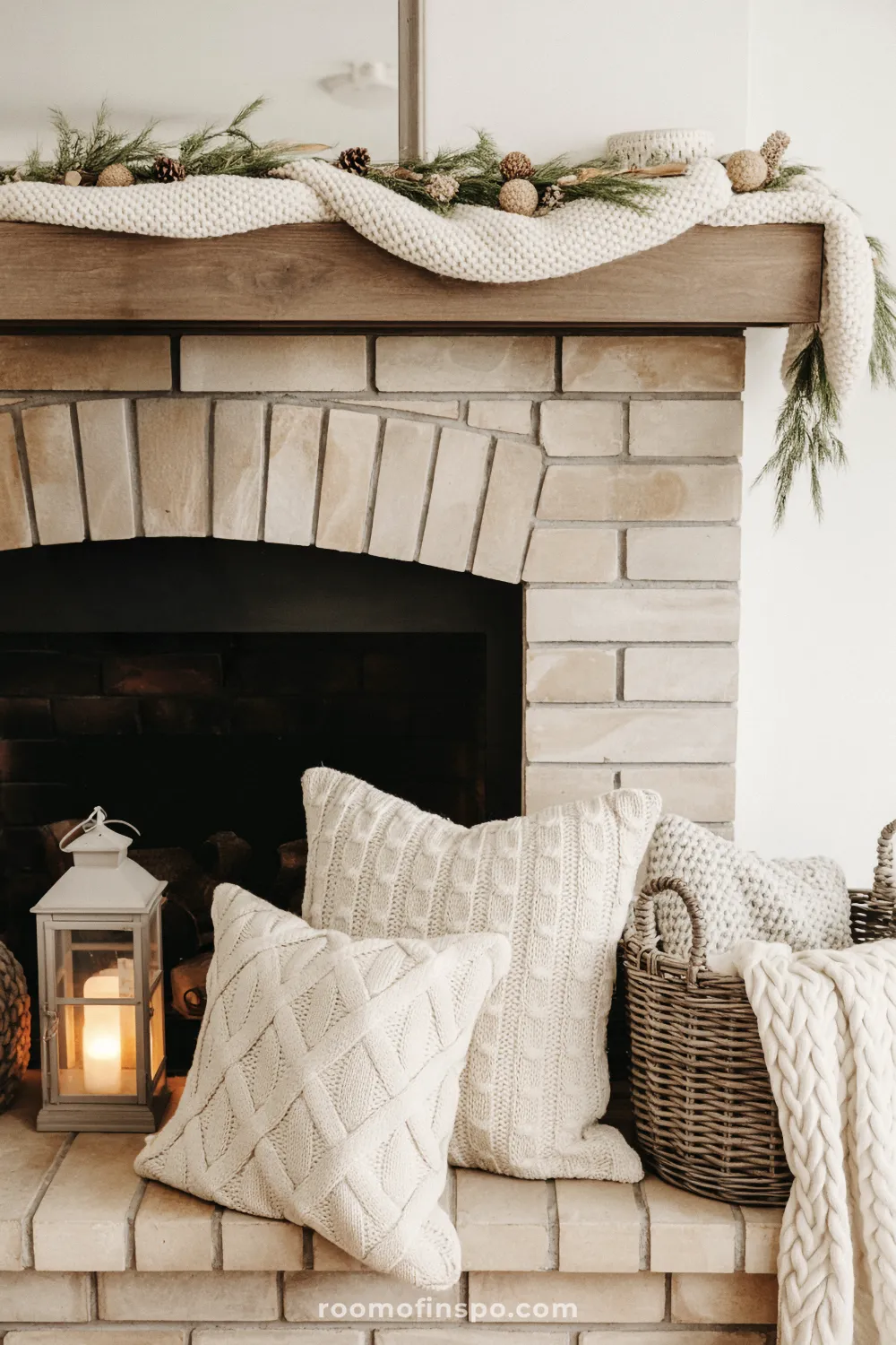 Rustic fireplace with brick arch and wood mantel decorated with a chunky knit garland, pinecones, and evergreen sprigs for holiday cheer.
