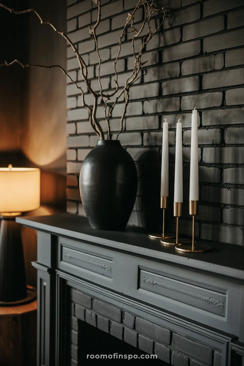 Rustic black painted brick fireplace and gray mantel decorated with a smooth black vase of bare branches and modern gold candlestick holders.