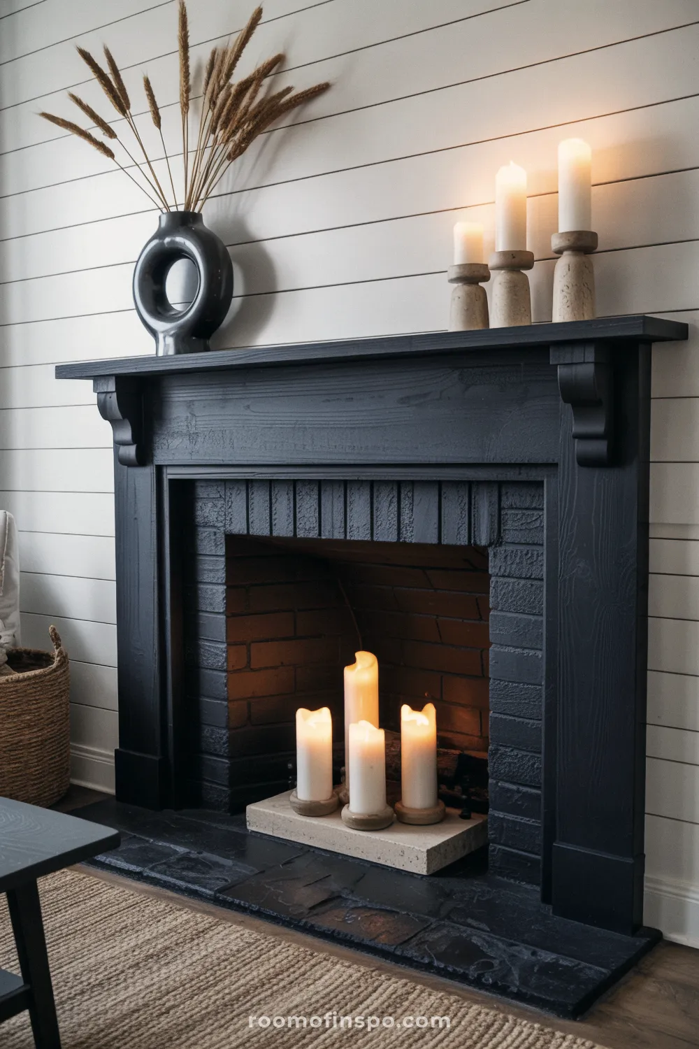 Farmhouse black painted wood fireplace and mantel with shiplap background, displaying dried reeds in a black vase and pillar candles.