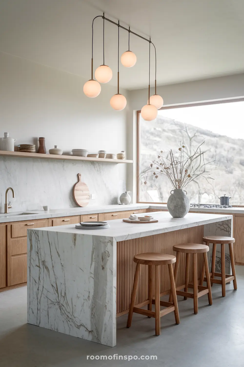 A modern Scandinavian kitchen with a large marble island, wooden stools, minimalist decor, and a unique hanging light fixture with six spherical bulbs.
