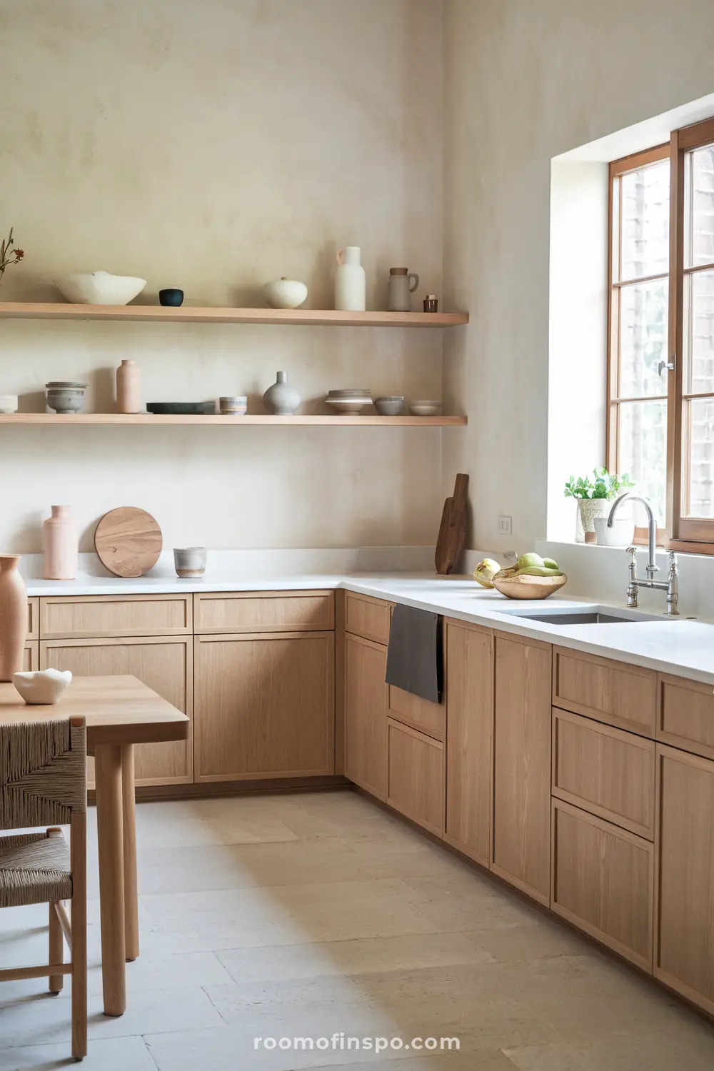 A modern Scandinavian kitchen with open shelving filled with ceramic bowls and plates, a minimalist countertop adorned with decorative items including a vase with green leaves, and a built-in oven on the right side, showcasing a clean and natural design.