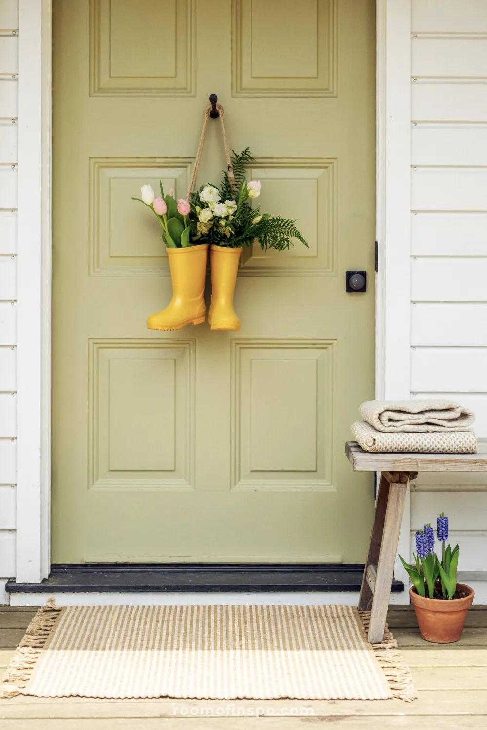 Sage door with yellow rain boot planters, a weathered bench, and layered striped rug with charcoal doormat.