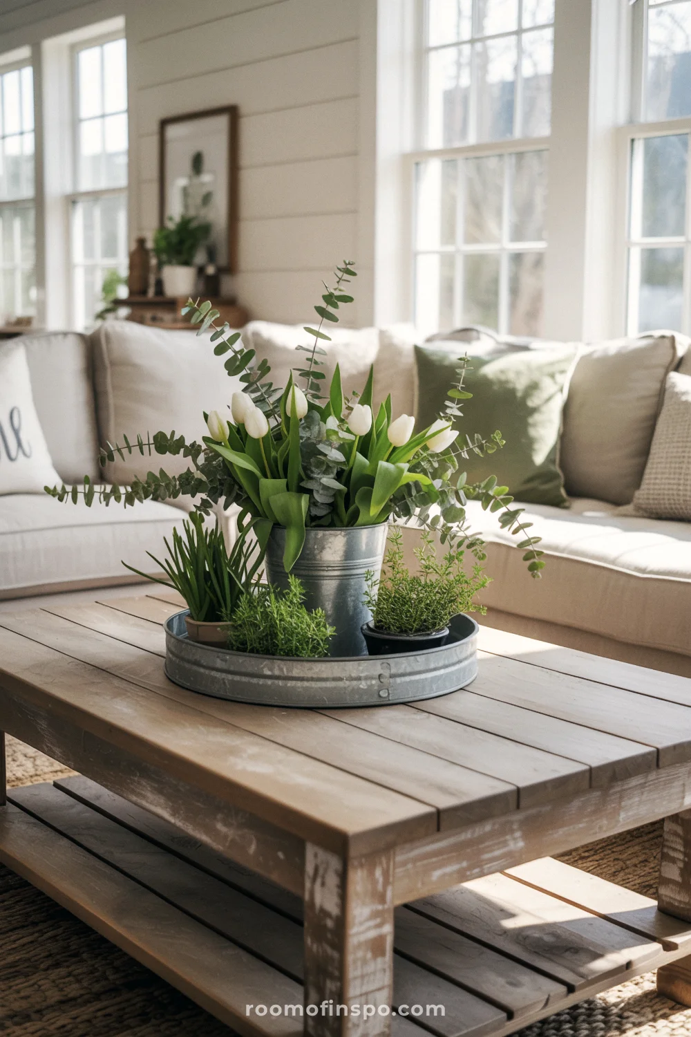 Rustic spring centerpiece with eucalyptus, white tulips, and herbs on a weathered wood coffee table in a farmhouse living room.