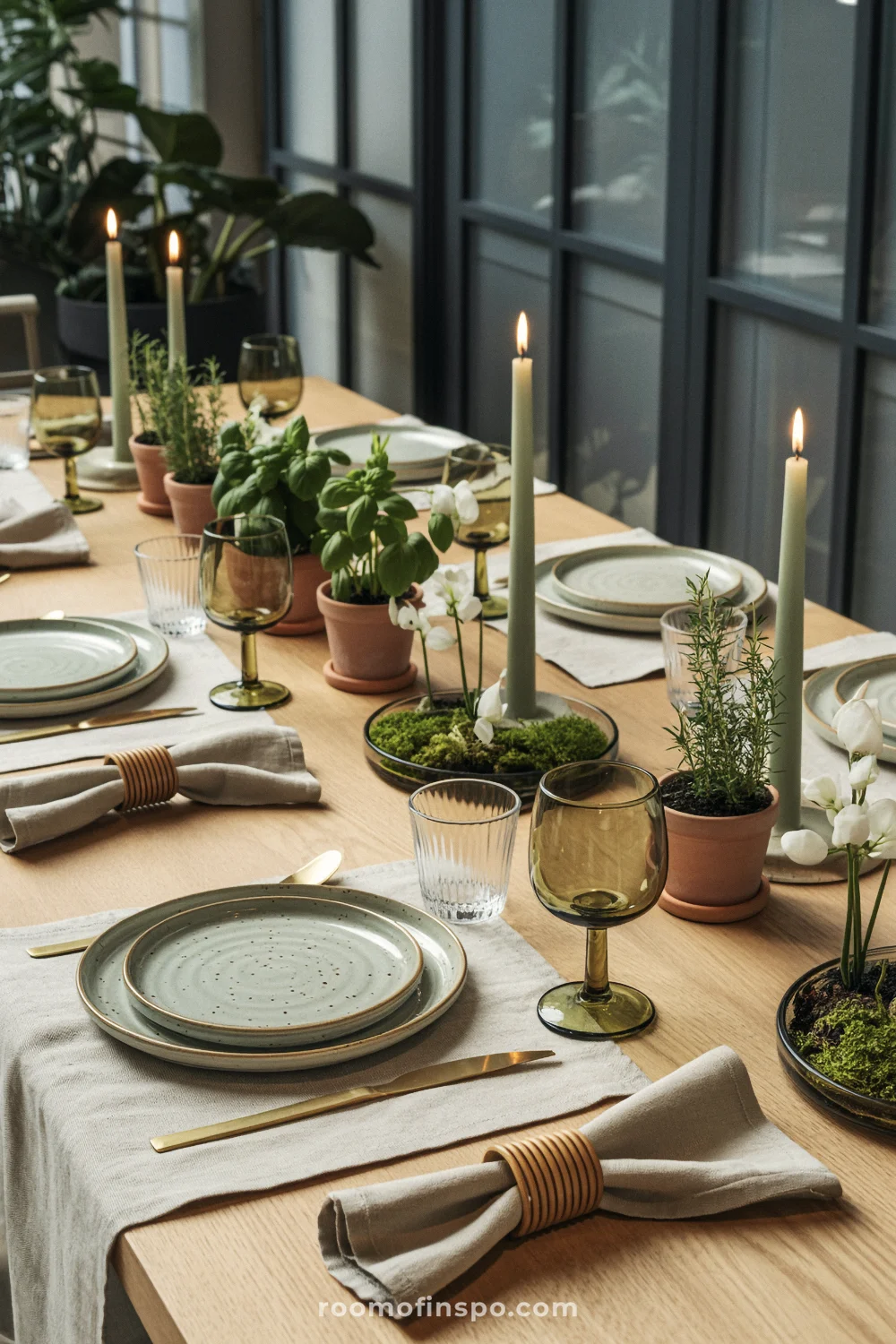 Table with potted herbs, moss bowls, sage plates, green goblets, and slim candles in clear holders.