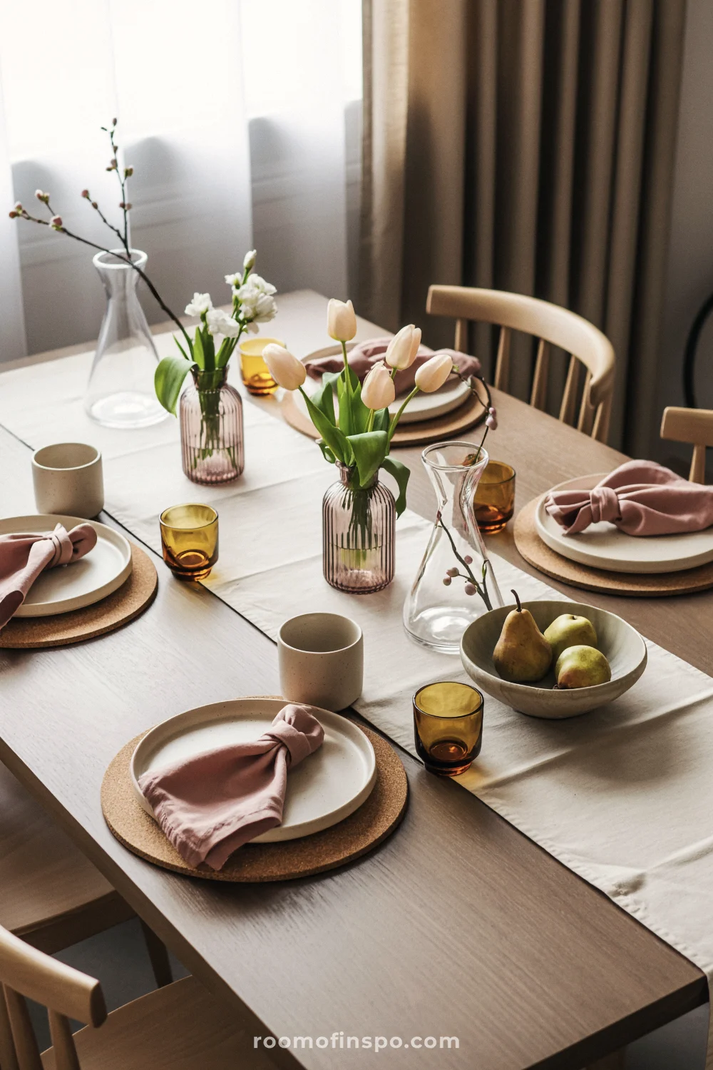 Walnut table with cork placemats, blush napkins, ribbed vases of tulips, and amber votives in window light.