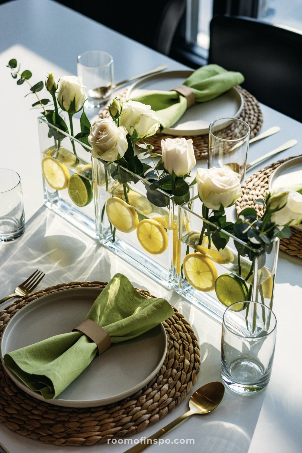 Three low glass vases lined with citrus slices and white roses, with seagrass placemats and pale green napkins.