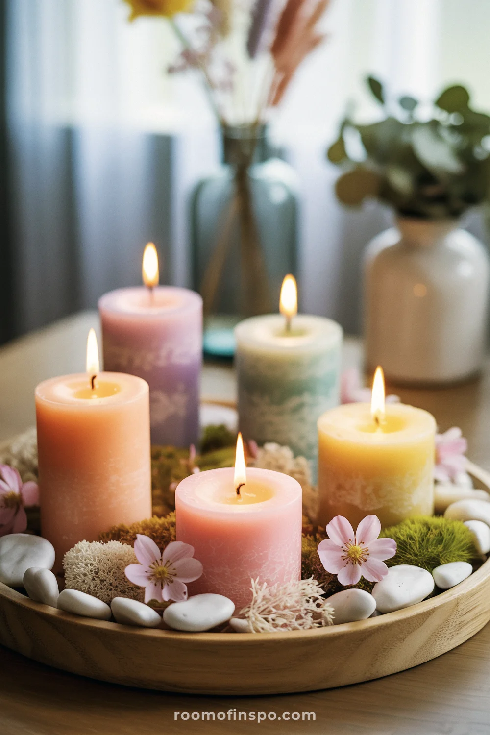 Pastel spring candle centerpiece with glowing pillar candles, pink blossoms, and natural textures on a wooden tray.