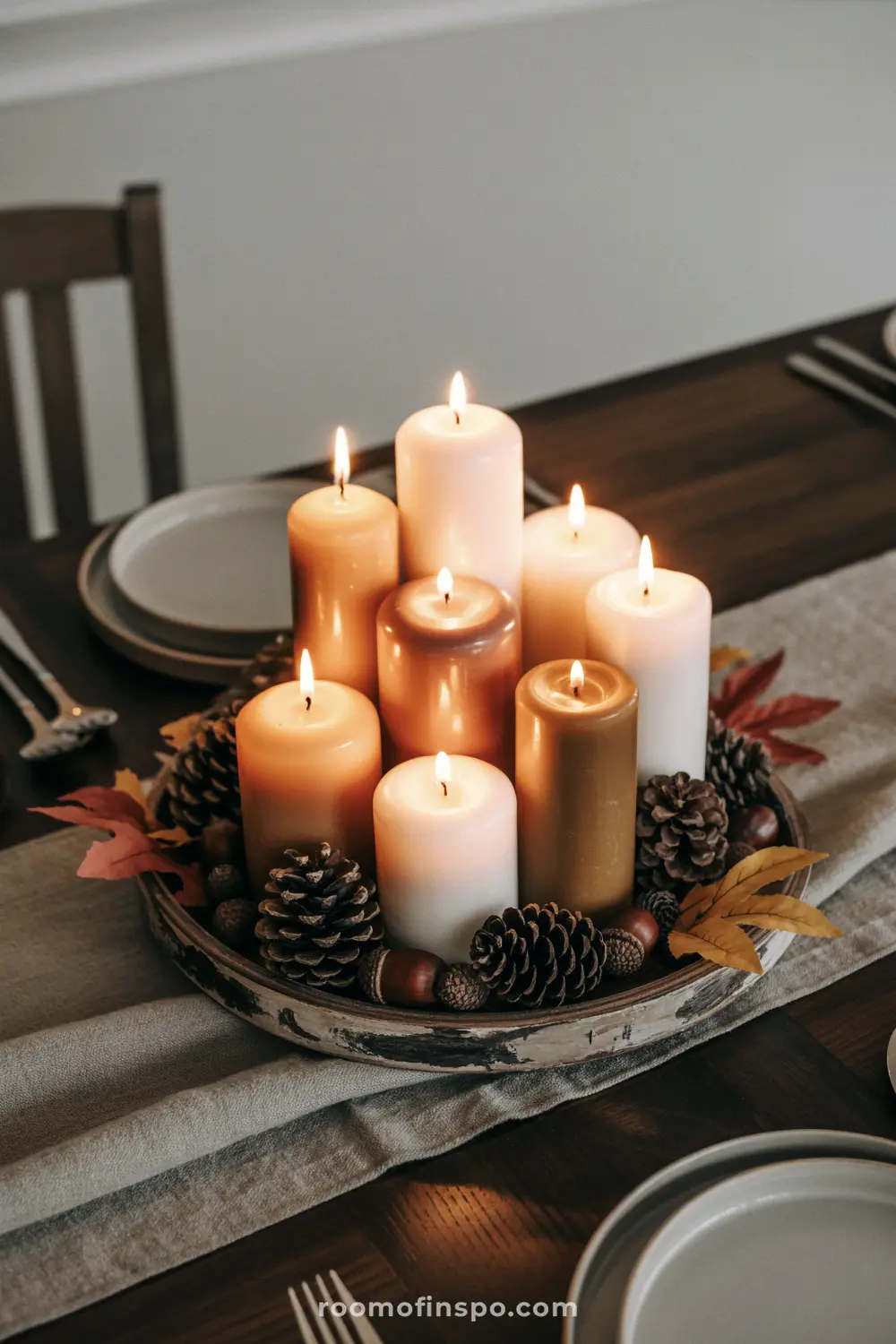 A stunning Fall centerpiece with a cluster of various-sized lit candles, surrounded by pine cones and autumn leaves.