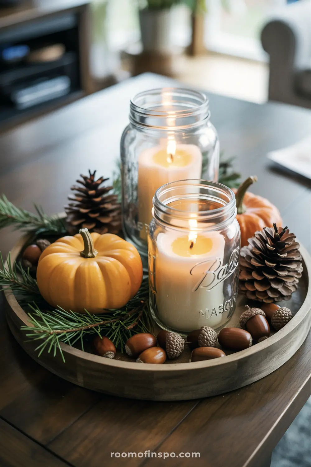 A simple Fall centerpiece on a wooden tray with mason jar candles, small pumpkins, pine cones, and acorns.