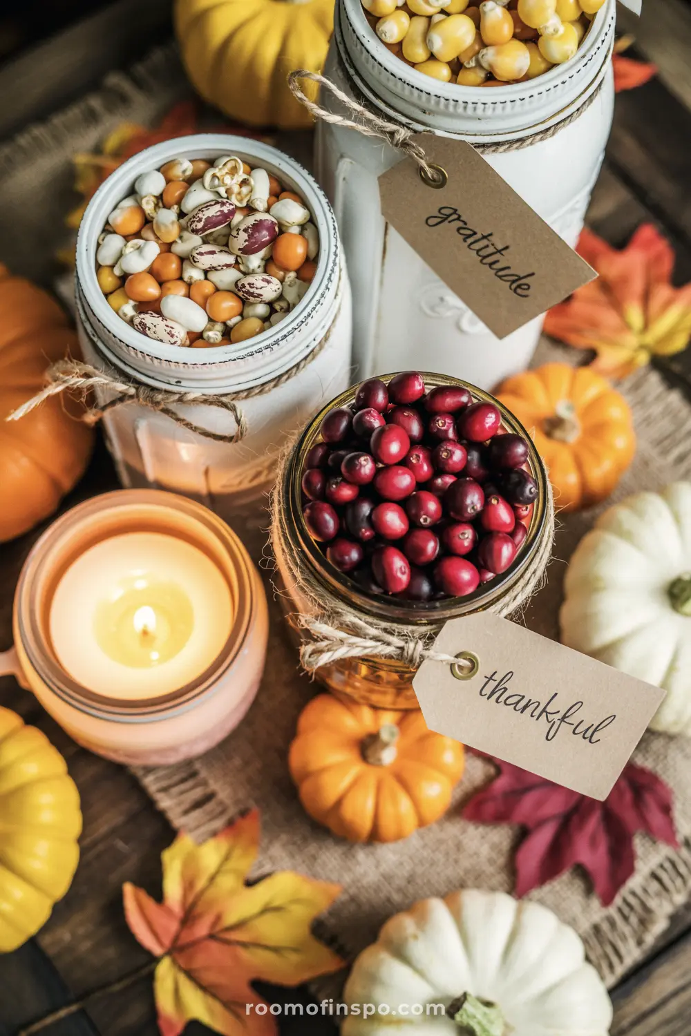 A charming Fall centerpiece with mason jars filled with cranberries and corn, pumpkins, and a lit candle.