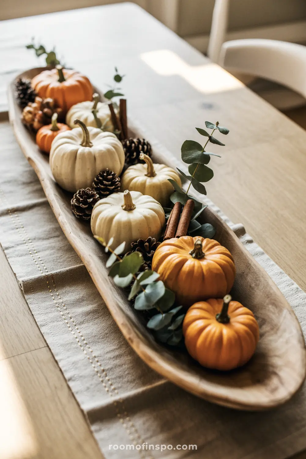 A simple Fall centerpiece with miniature pumpkins, pine cones, and eucalyptus branches in a long wooden dough bowl.