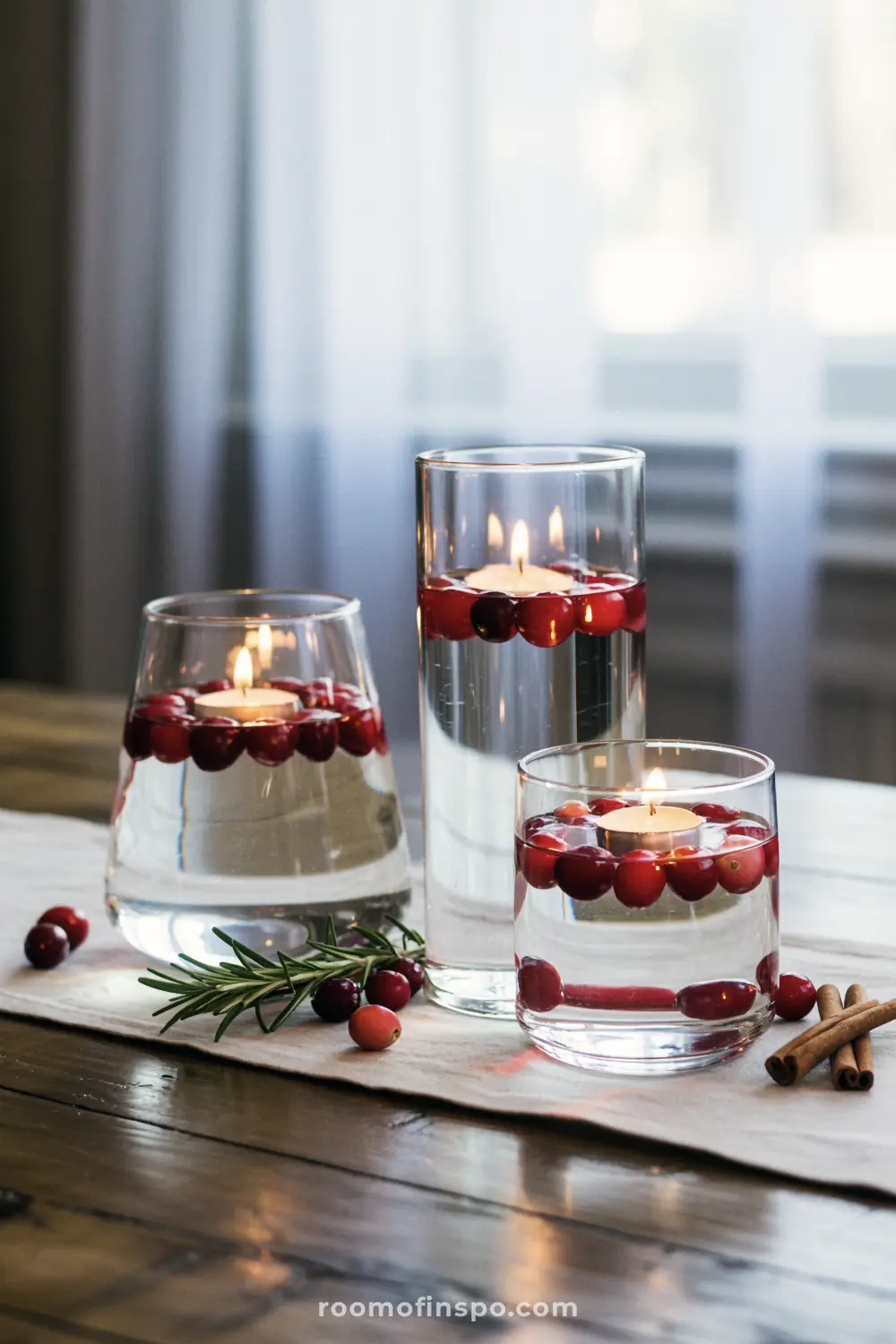 A minimalist Fall centerpiece with floating candles and cranberries in three glass vases on a table runner.