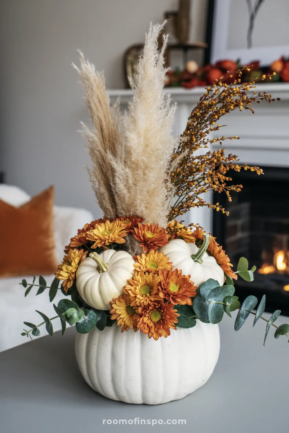 A creative Fall centerpiece with a white pumpkin serving as a vase, holding flowers, miniature pumpkins, and pampas grass.