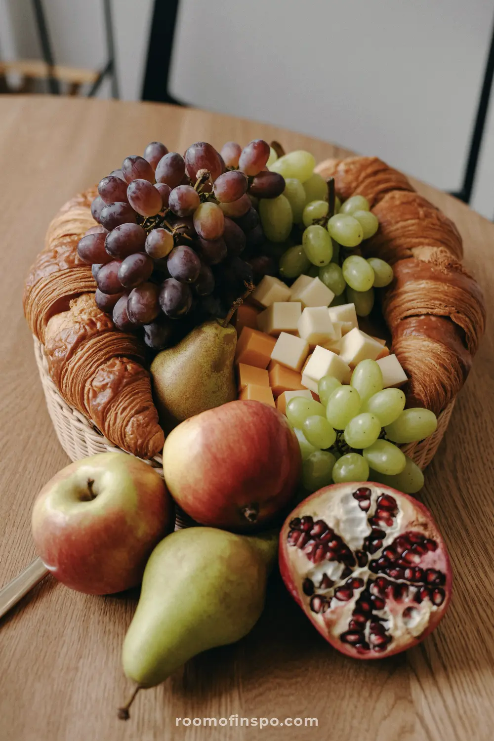 A simple Fall centerpiece featuring a wicker basket filled with croissants, cheese, grapes, apples, pears, and a pomegranate.