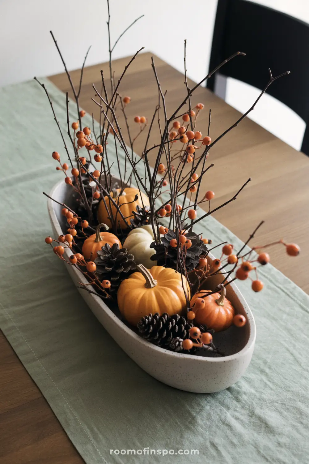 A charming Fall centerpiece with a long bowl filled with miniature pumpkins, pine cones, and branches with orange berries.