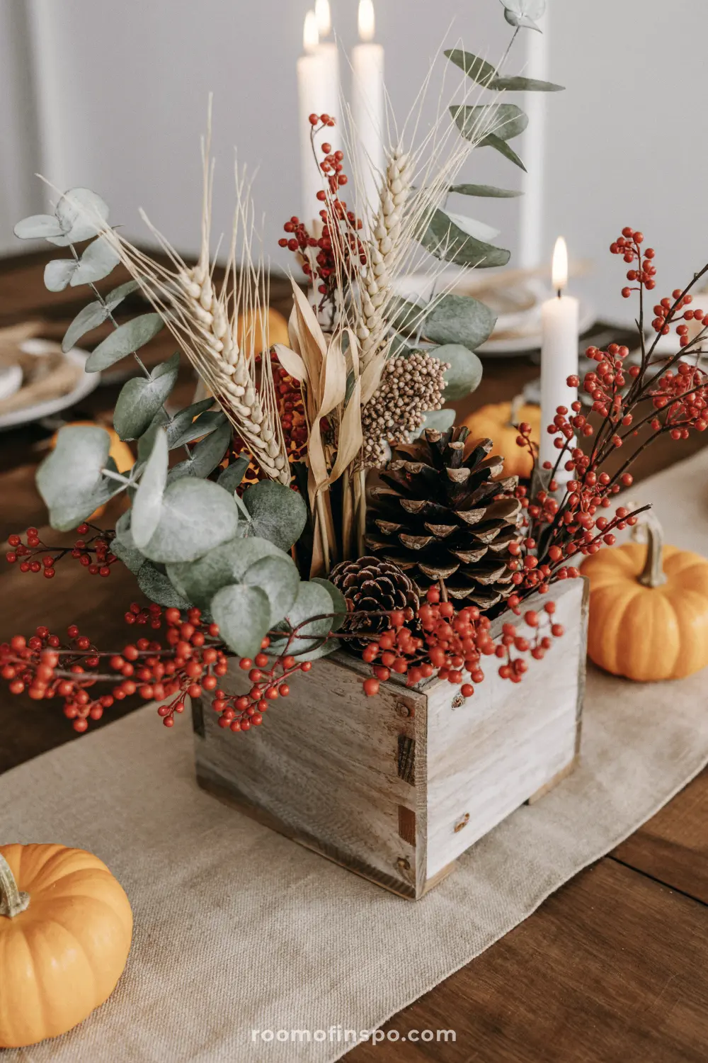 A festive Fall centerpiece in a rustic wooden box, with wheat, pine cones, red berries, and eucalyptus branches.
