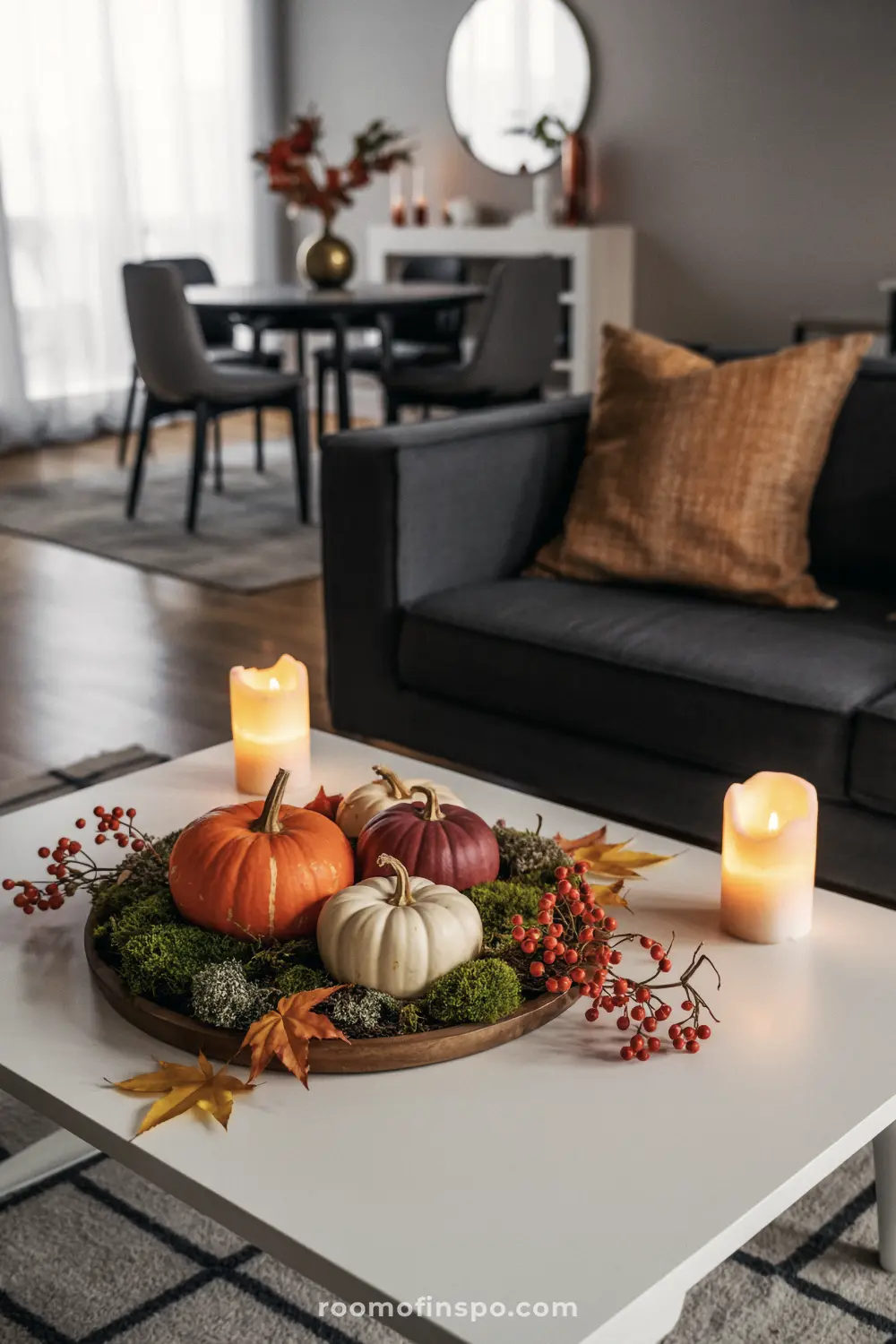 A festive Fall centerpiece with pumpkins, moss, red berries, and leaves on a round wooden tray on a coffee table.