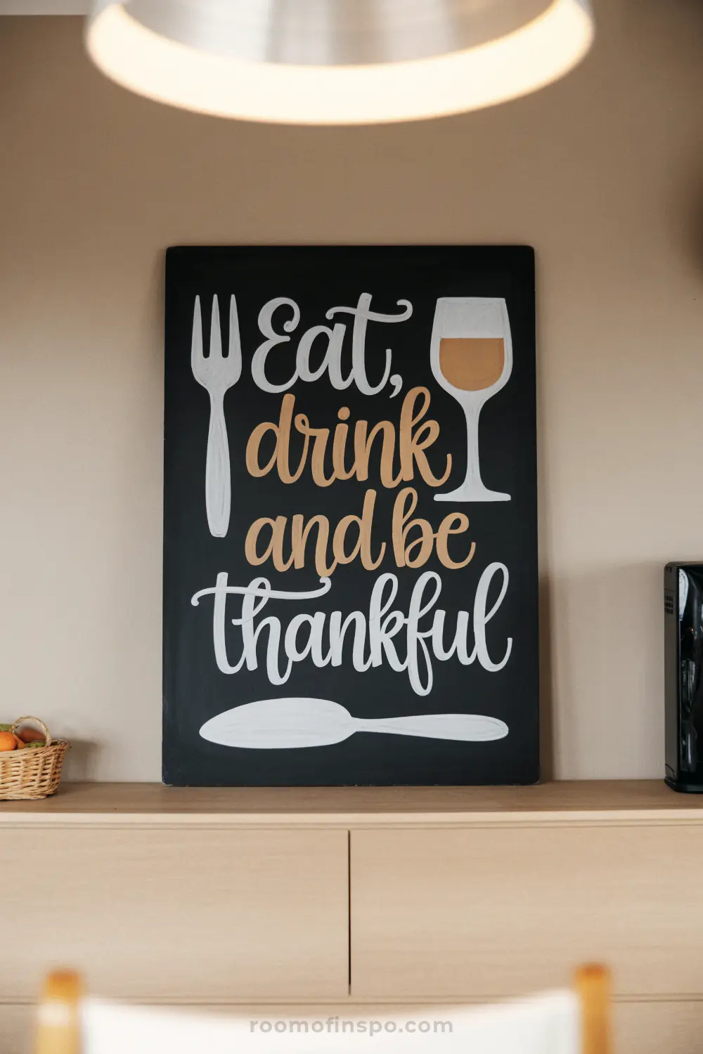 A dark chalkboard with a Thanksgiving message "Eat, drink and be thankful" alongside a fork, spoon, and wine glass.