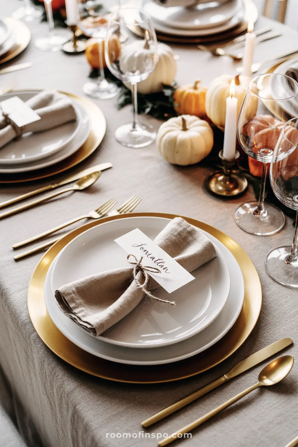 An elegant thanksgiving place setting with gold chargers, white plates, and a handwritten name card tied with twine.