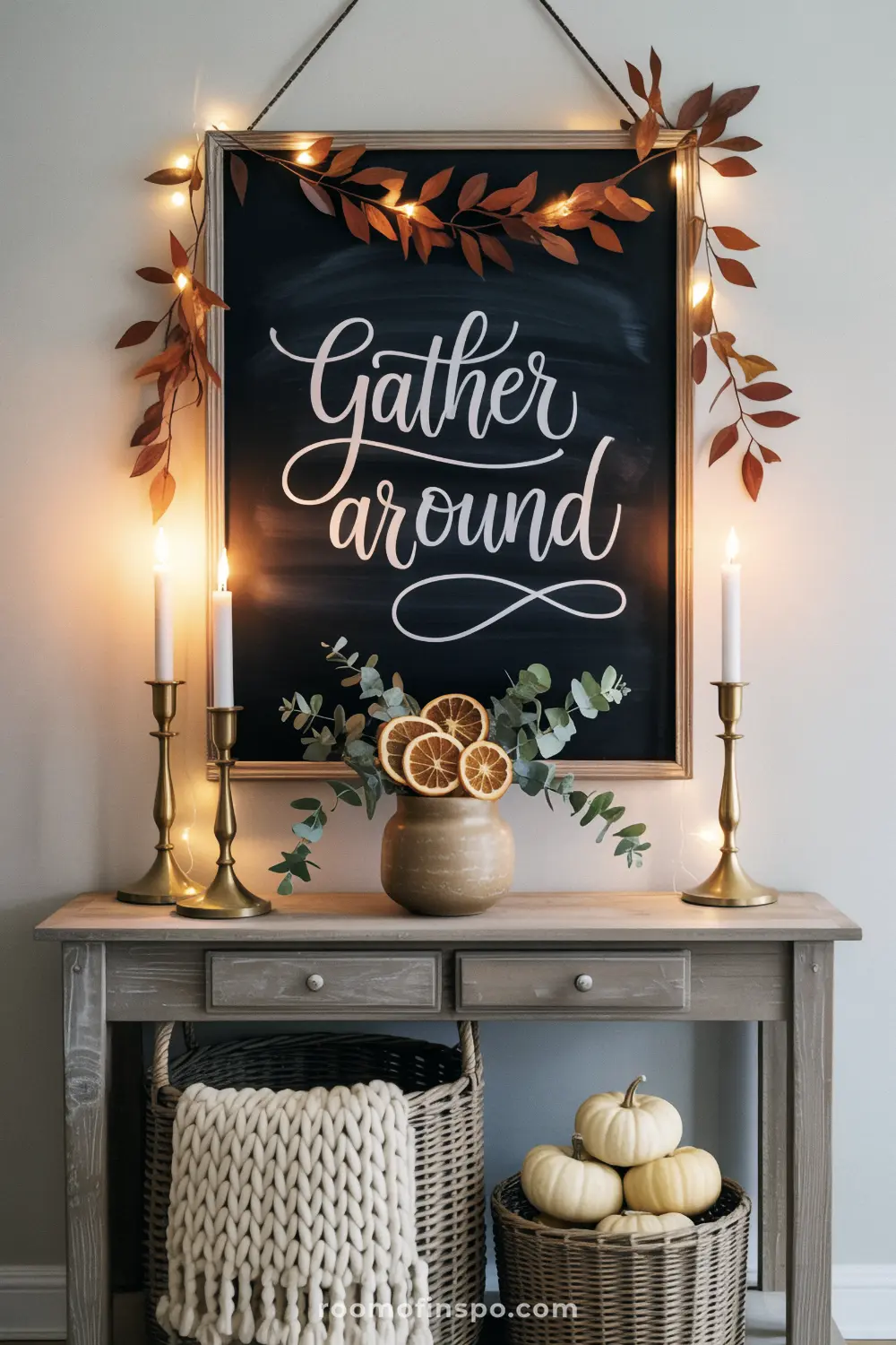 A thanksgiving-themed chalkboard with "Gather around" in calligraphy, surrounded by string lights and candles on a wooden console.