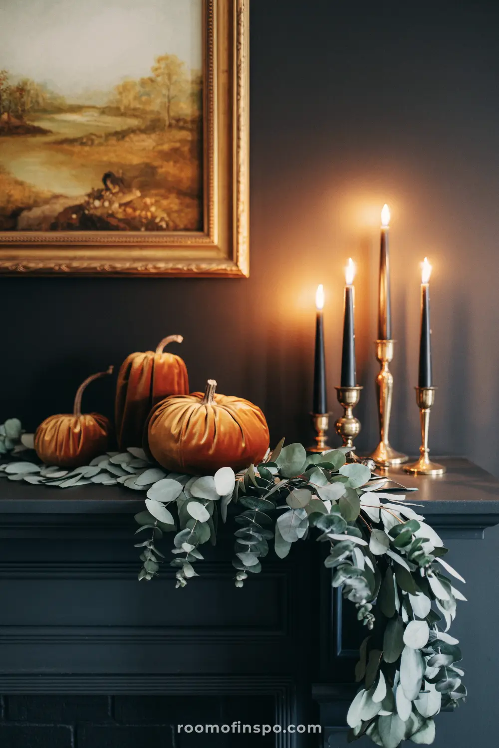 A thanksgiving mantelpiece with velvet pumpkins, black candles in gold holders, and a eucalyptus garland.