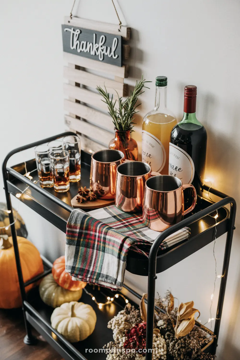 A black bar cart decorated for thanksgiving with copper mugs, bottles of beverages, and a "thankful" sign.