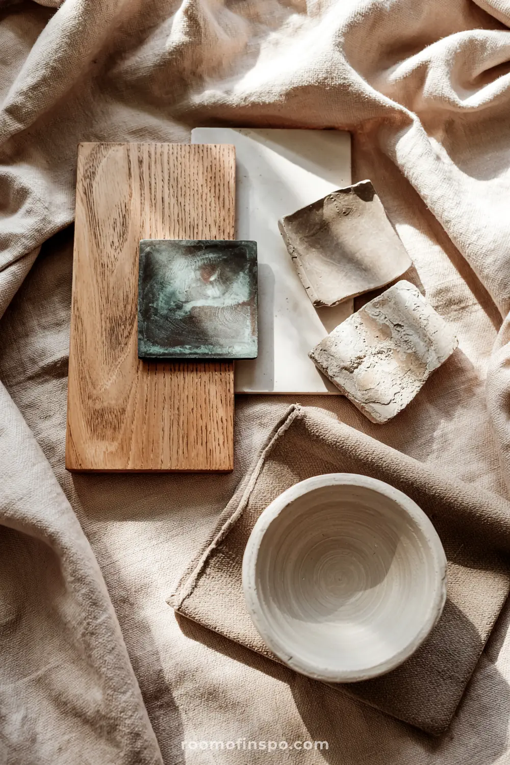 Wabi Sabi bathroom with a collection of wooden boards, white tiles, metallic tiles, textured stone pieces, and a ceramic bowl arranged on a beige fabric surface.