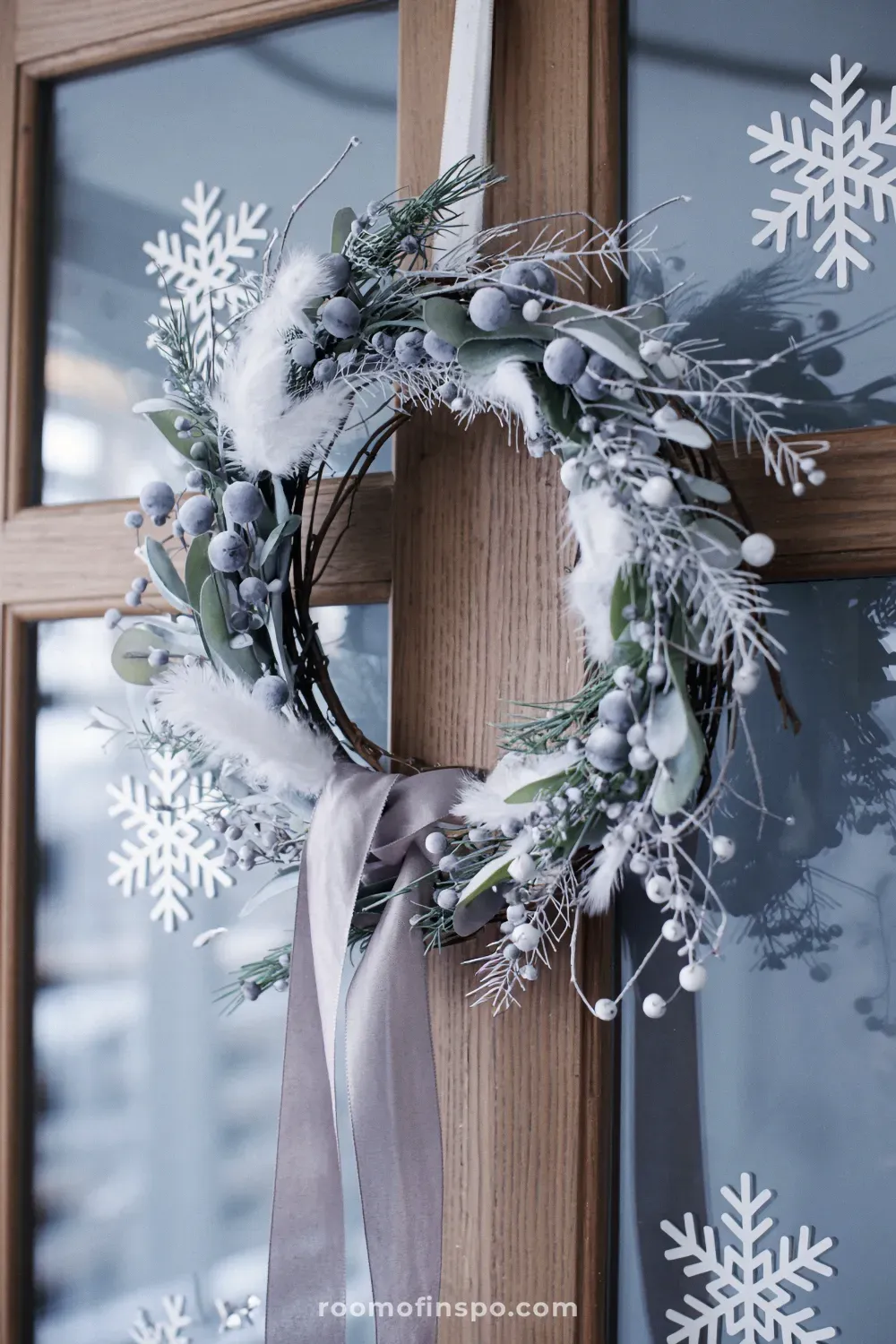 Elegant winter decor wreath with frozen berries and white accents hanging on a door with snowflake decals.