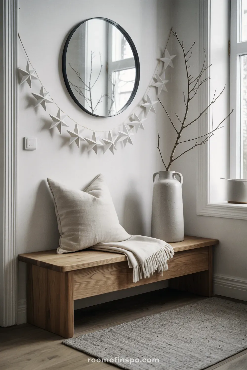 Minimalist entryway bench area displaying simple winter decor with bare branches and a white paper star garland.