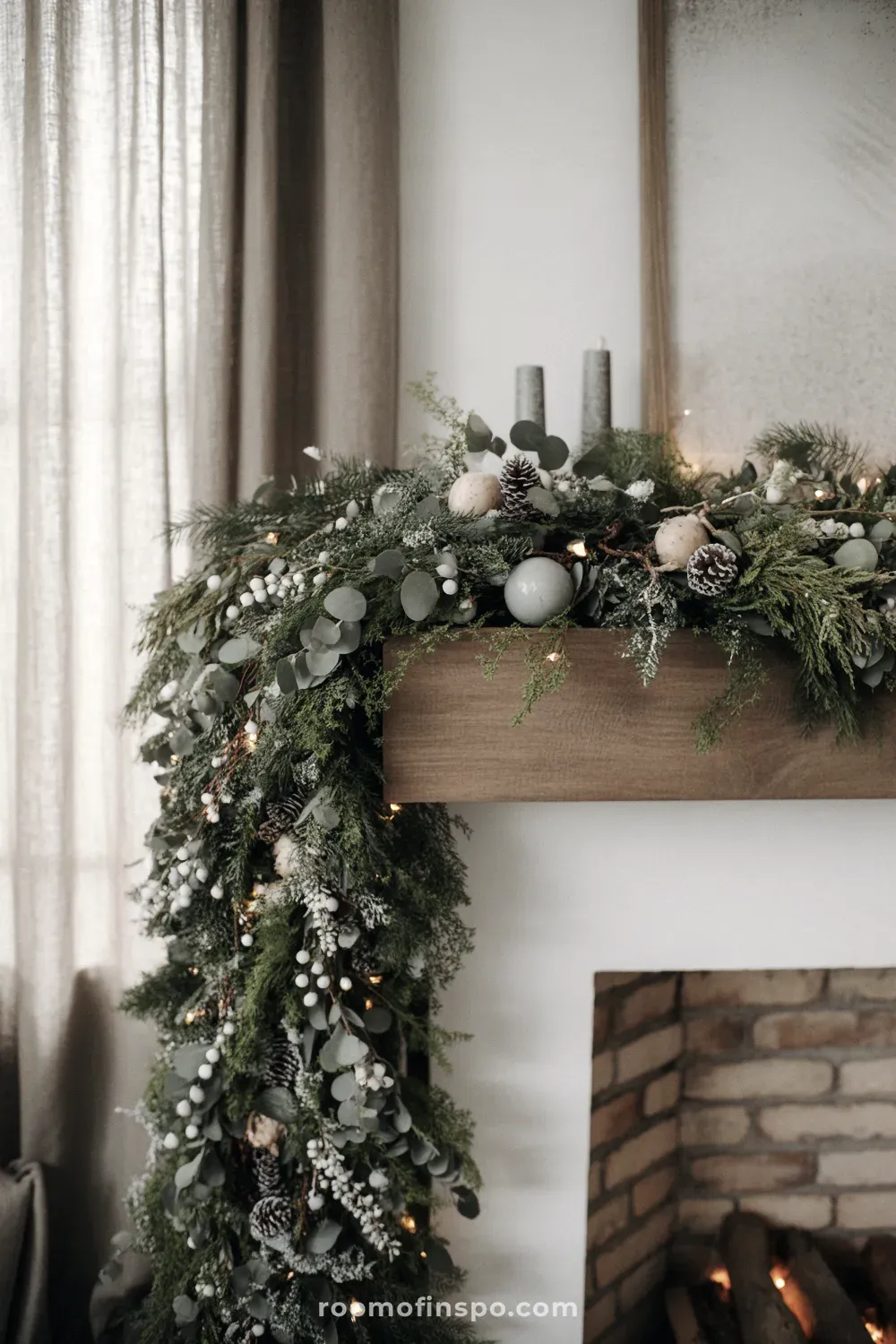 A rich, dark green winter garland covers a white fireplace mantel, extending down one side in an opulent design.