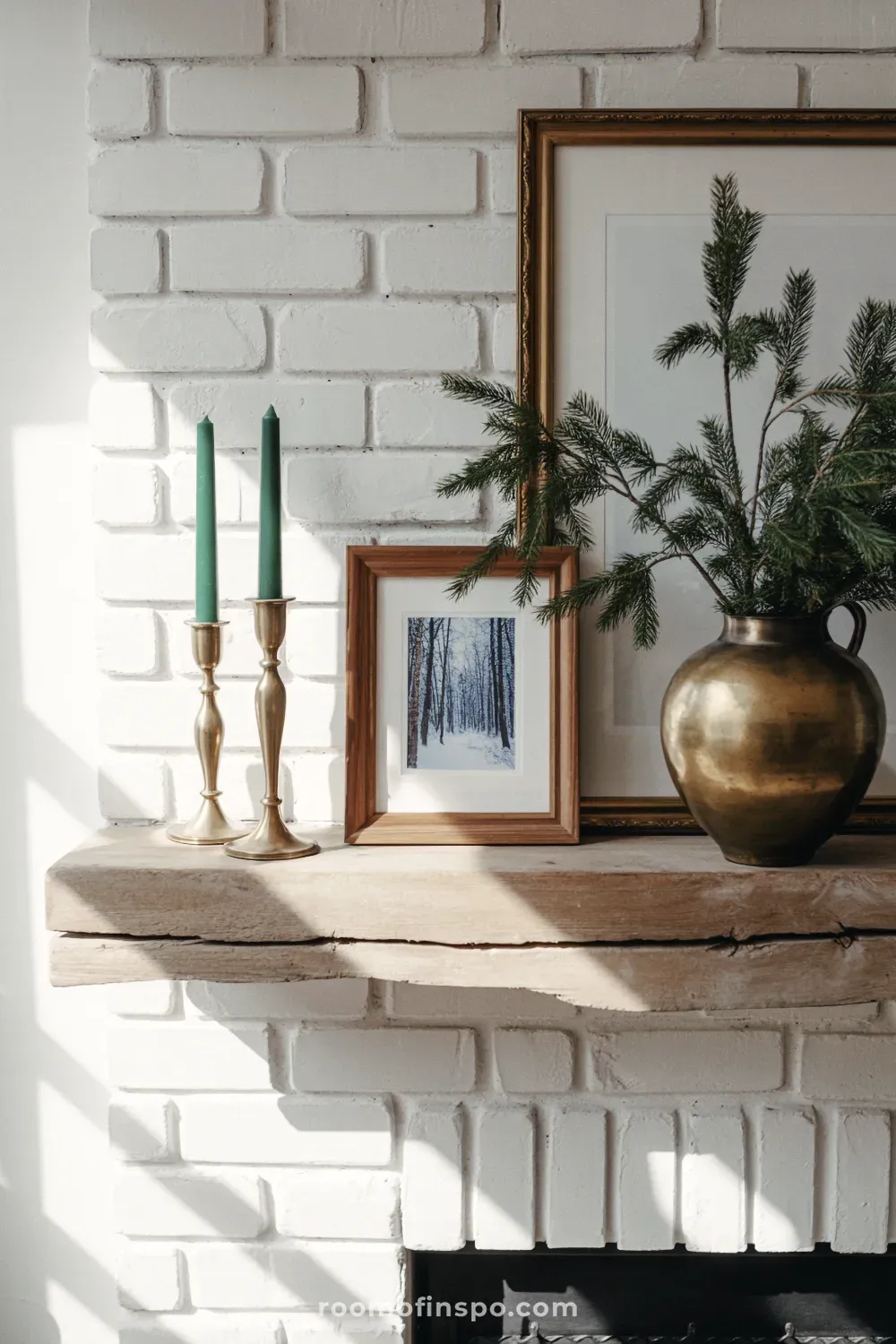 A cozy, rustic winter look with pine branches and a framed picture on a brick fireplace mantel in bright sunlight.