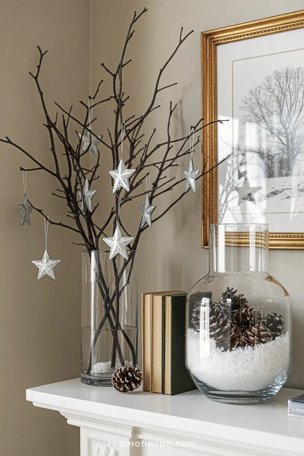 Bare winter branches are held in a tall vase next to a framed picture on a rustic wood fireplace mantel decorated with silver.