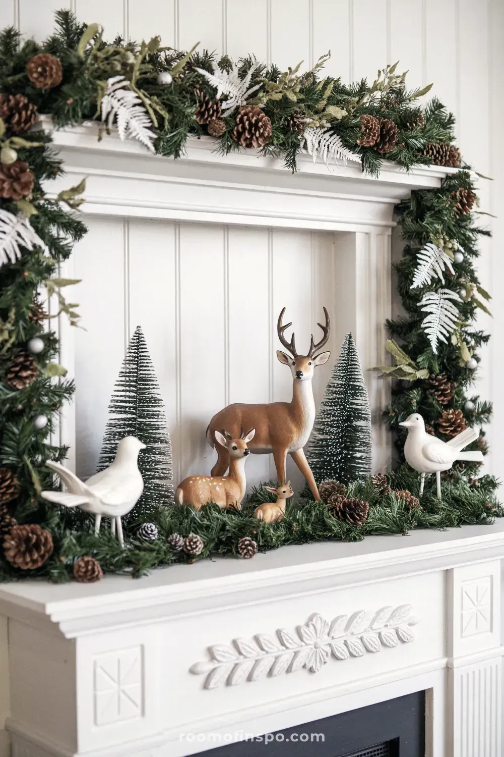 A charming woodland winter wonderland featuring a deer and festive trees arranged on a white stone fireplace mantel.