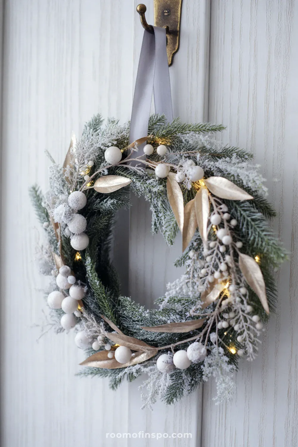 A mixed-material winter wreath with gold accents and dark berries, giving it a festive and elegant look on a white door.