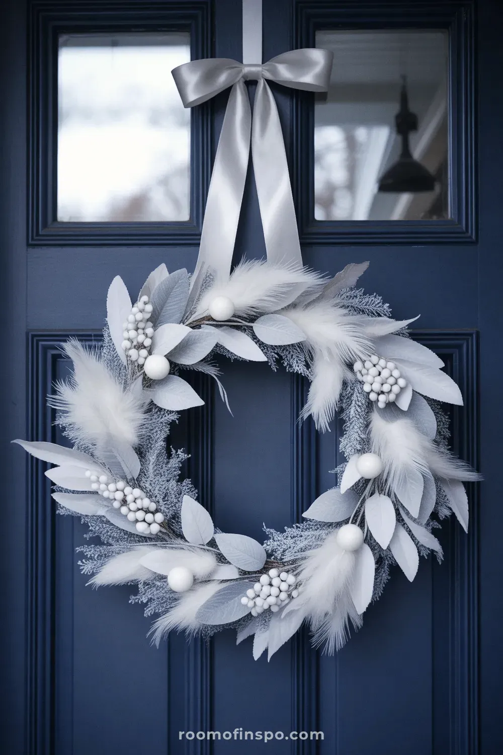 An elegant winter wreath of silvery-blue foliage and white berries, offering a cool-toned, frosty aesthetic on a dark blue door.