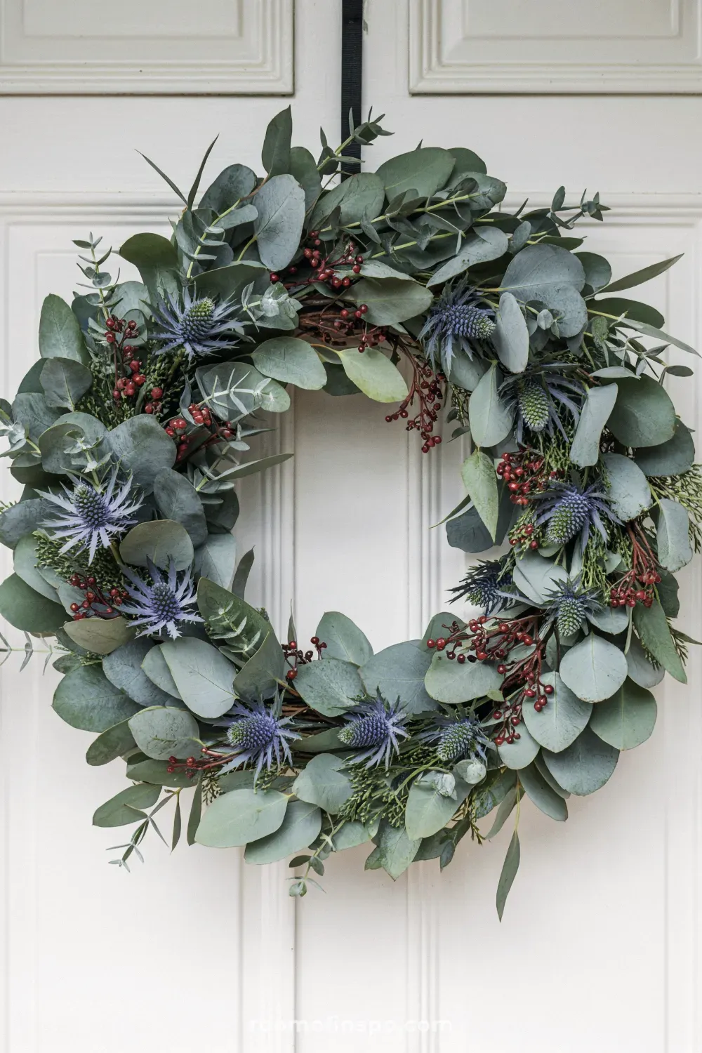 A lush, deep green winter wreath with pinecones and red berries, presenting a classic and full, traditional appearance.