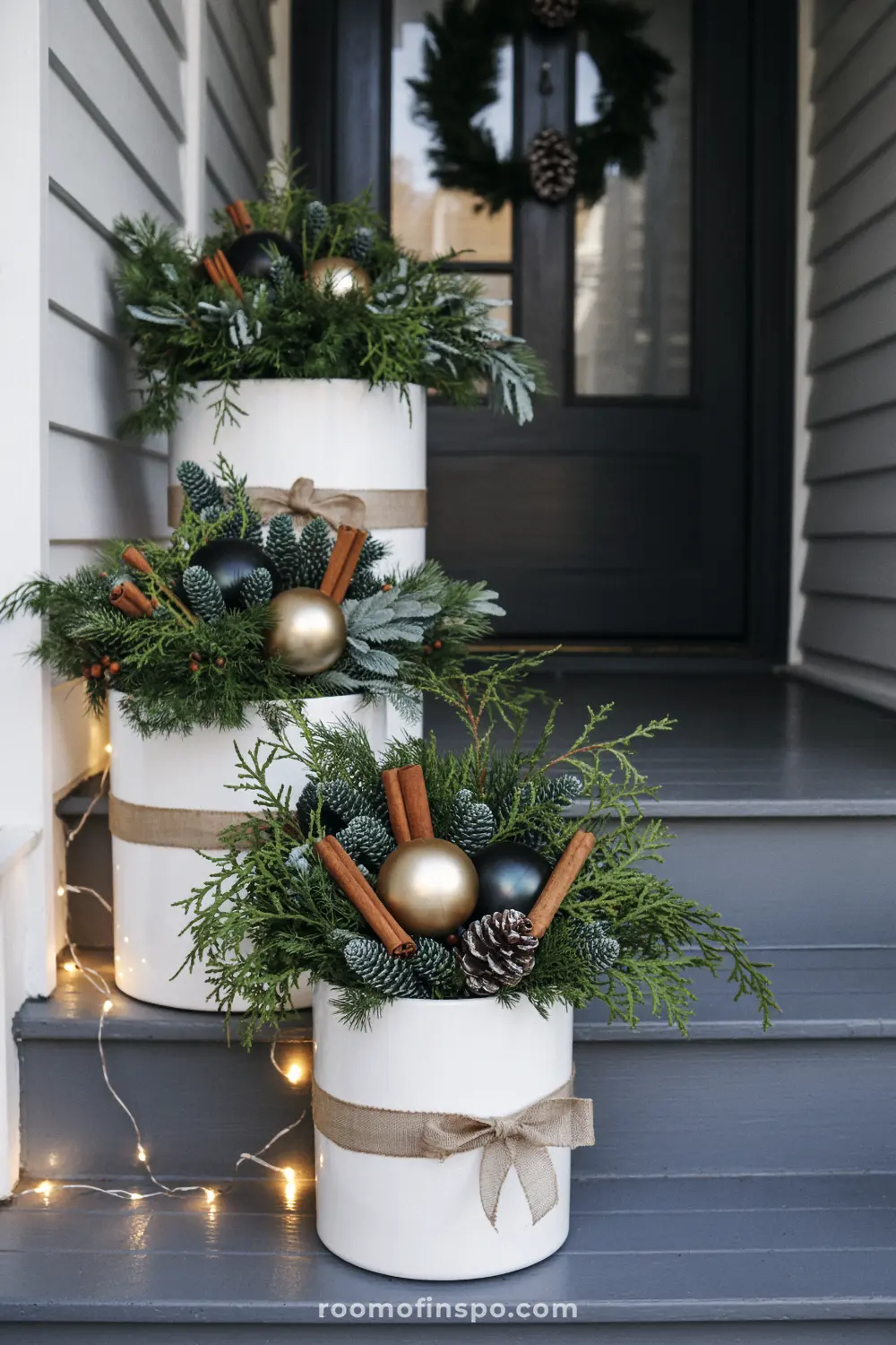Tiered white pots with greenery and cinnamon sticks on a porch stairway, decorated for Christmas.