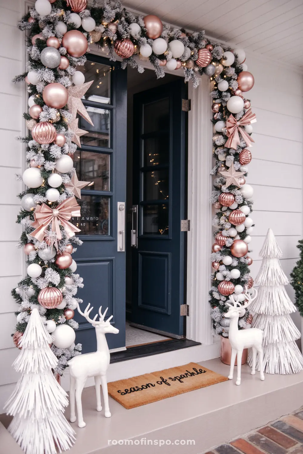A modern front porch with white deer and a Christmas archway of garland and rose gold ornaments.
