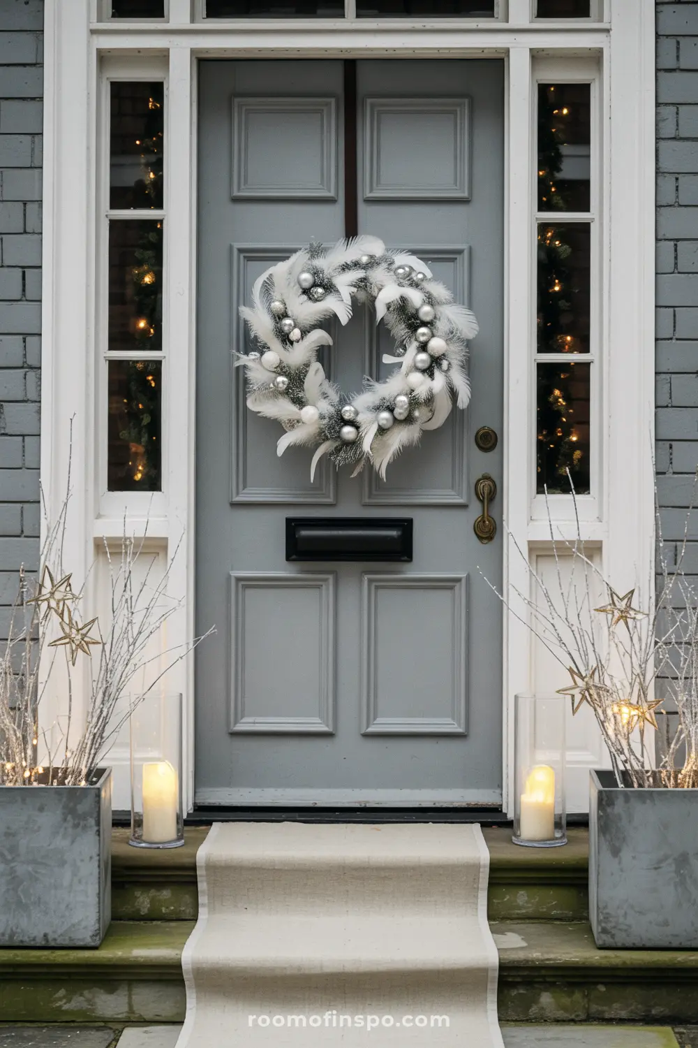 A chic, minimalist front porch with a white feather Christmas wreath and glowing lights in planters.