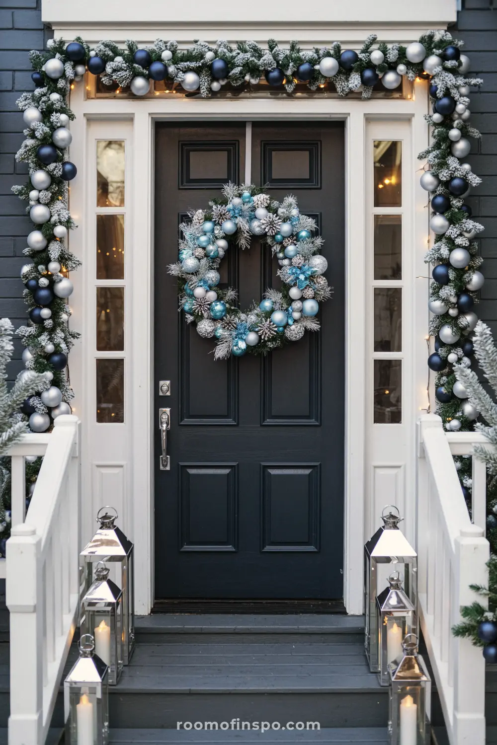A frosted Christmas wreath and garland with blue and silver ornaments on a dark gray front porch.