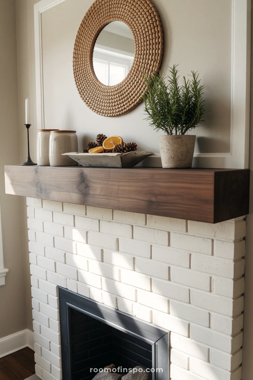 White brick fireplace with dark walnut mantel, rattan mirror, ceramic crocks, and a dough bowl centerpiece.