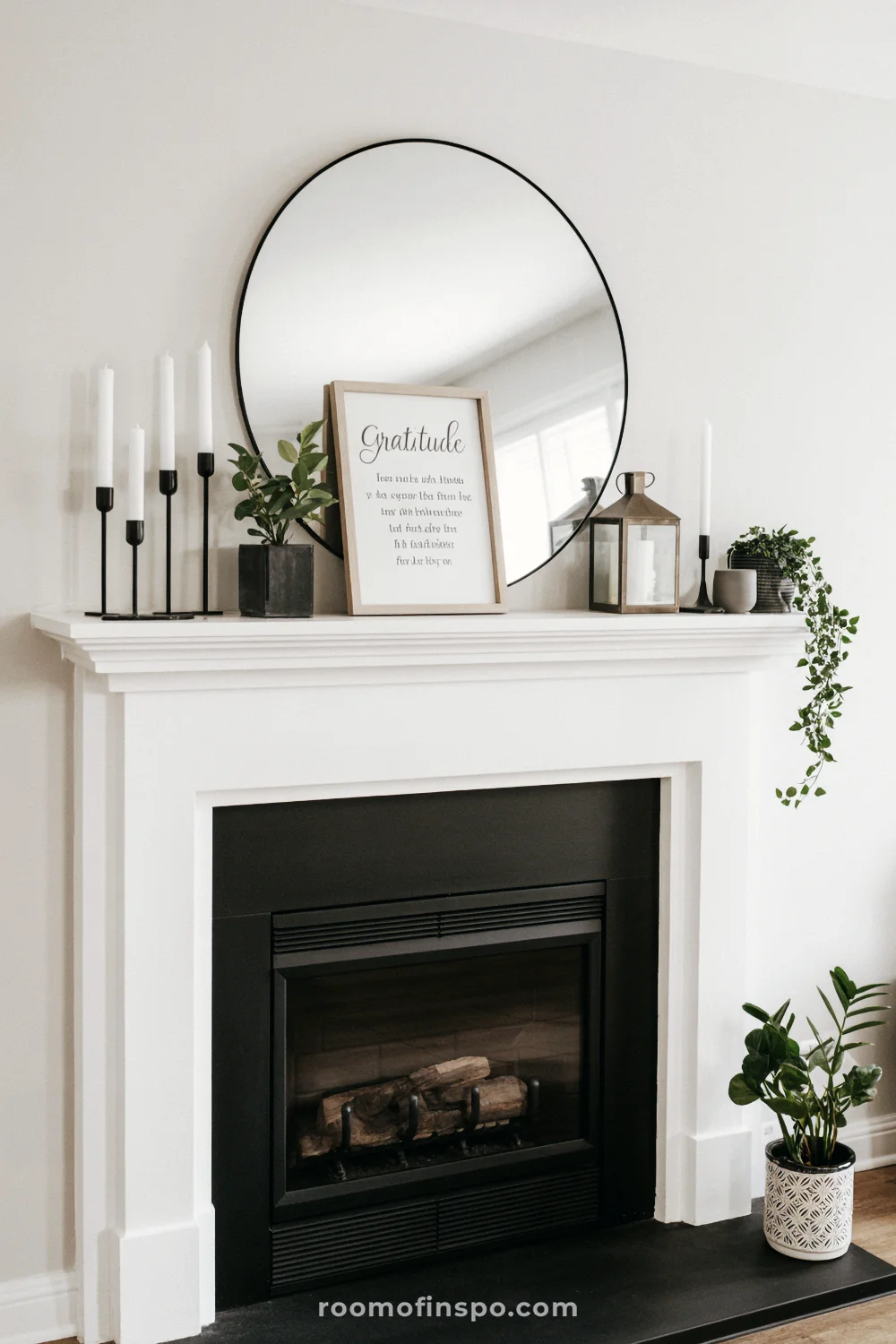 White mantel with round black-framed mirror, black candleholders, greenery, and a lantern near the hearth.