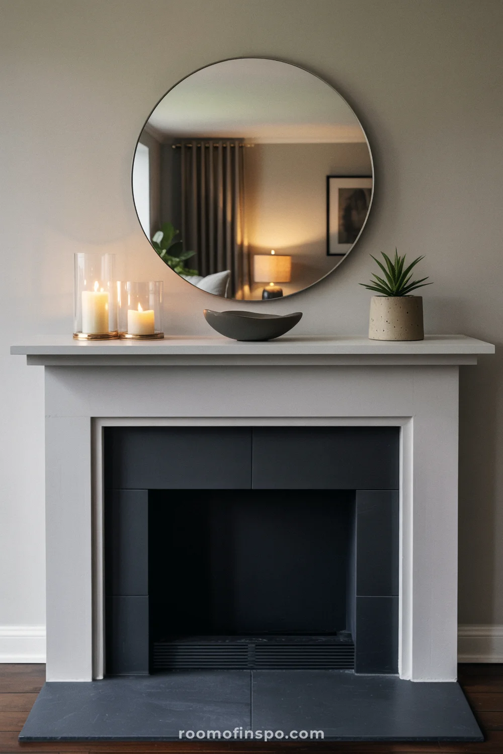White mantel with polished nickel round mirror, three glass hurricanes, a small succulent, and slate hearth.