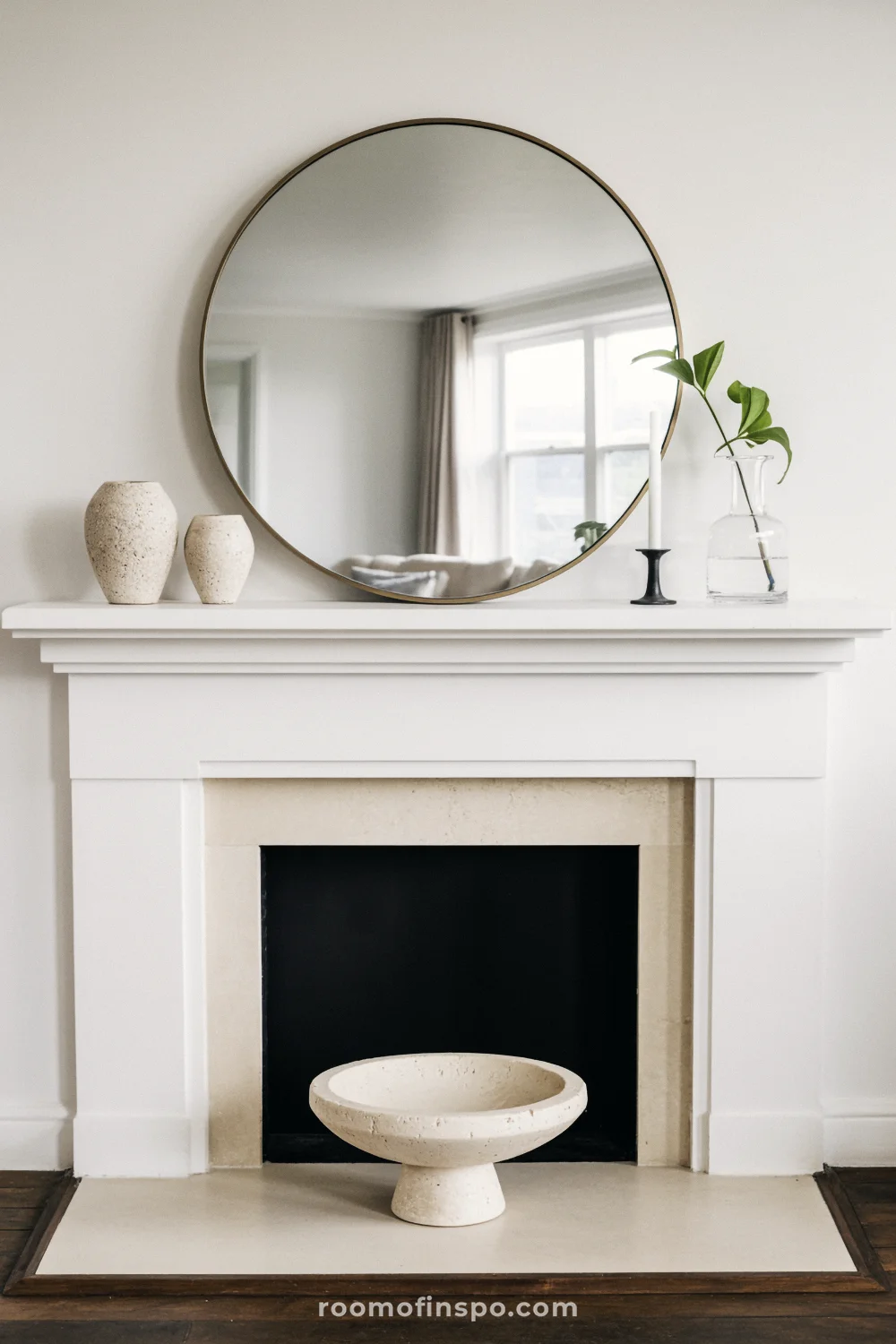 White mantel with round brass mirror, two cream ceramics, a small candlestick, and a single-stem vase.