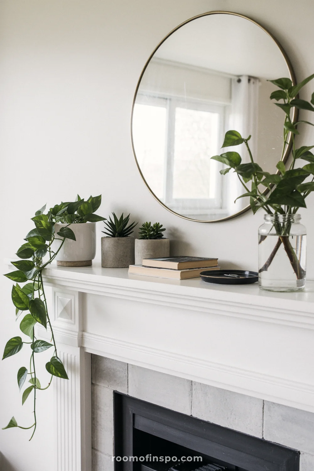 White mantel with brass round mirror, small potted plants, trailing pothos, and glass jar clippings.